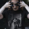 Das Bild zeigt eine nähere Aufnahme der mystischen Frau die das schwarze T-Shirt mit dem Vampir Kuss Design trägt. Es wird verwendet, um einen Eindruck zu vermitteln, wie das Produkt an einem Menschen aussieht.