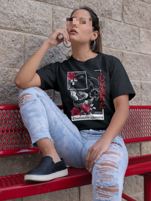 Das Bild zeigt eine sitzende Frau die das schwarze T-Shirt mit dem Kanji Skull Design trägt. Es wird verwendet, um einen Eindruck zu vermitteln, wie das Produkt an einem Menschen aussieht.