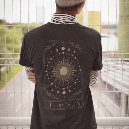 Das Bild zeigt einen Mann der das schwarze Tarot Card The Sun T-Shirt trägt. Es wird verwendet, um einen Eindruck zu vermitteln, wie der Rückendruck vom Produkt an einem Menschen aussieht.