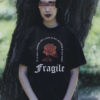 Goth-Girl trägt schwarzes Unisex Relaxed Fit T-Shirt mit Fragile Gothic Rose Design.